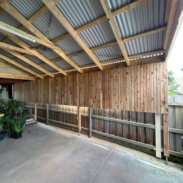 Timber carport with exposed rafters alongside a fence