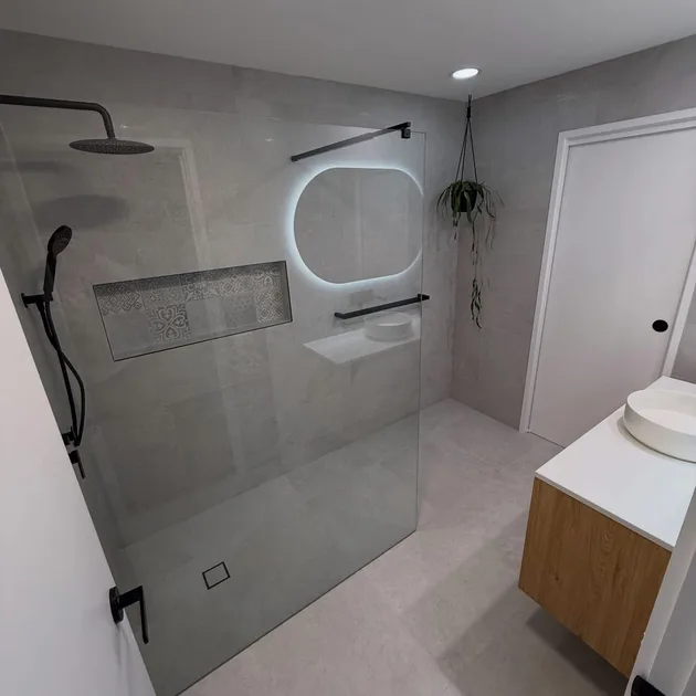 Grey tiled bathroom with a frameless shower screen and backlit mirror
